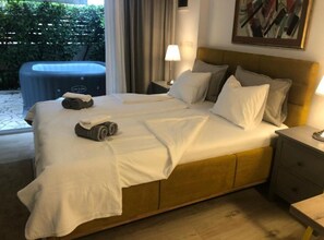 Ein Doppelbett mit weißen Bettwäsche, ein Holz-Kopfteil, ein Nachttisch mit Lampe und Blick auf Grünfläche.