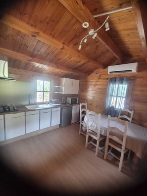 A wooden cabin with a kitchen, dining area, and an air conditioning unit.