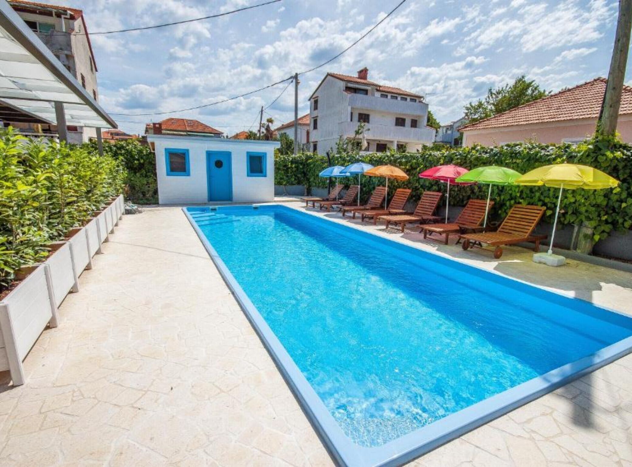 Piscina com espreguiçadeiras e guarda-sóis, rodeada por edifícios.
