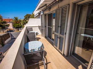 Ein Balkon mit Tisch und Stühlen, eine Schiebeglastür und ein kleiner Gartenbereich.