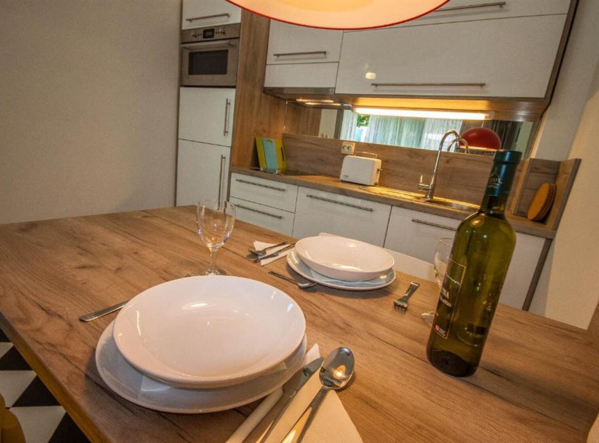 A kitchen with white cabinets, a wooden countertop, a wine bottle, and a glass.