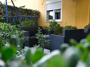 Een terras met rieten meubels, planten in potten en een gele muur.