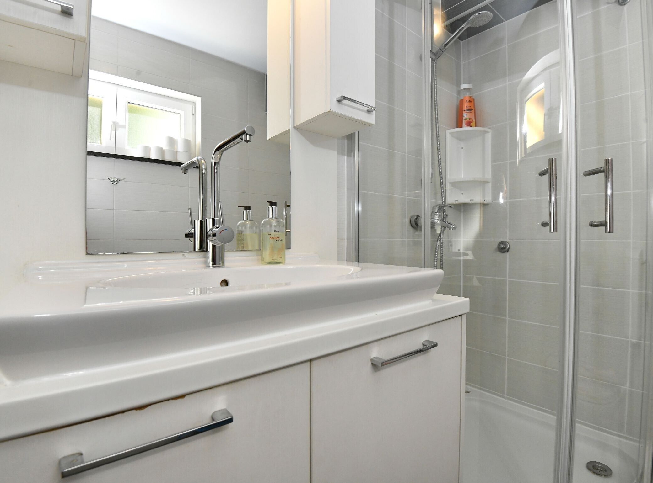 Een badkamer met een wit wastafelmeubel, een spiegel, een douchecabine en een kast.
