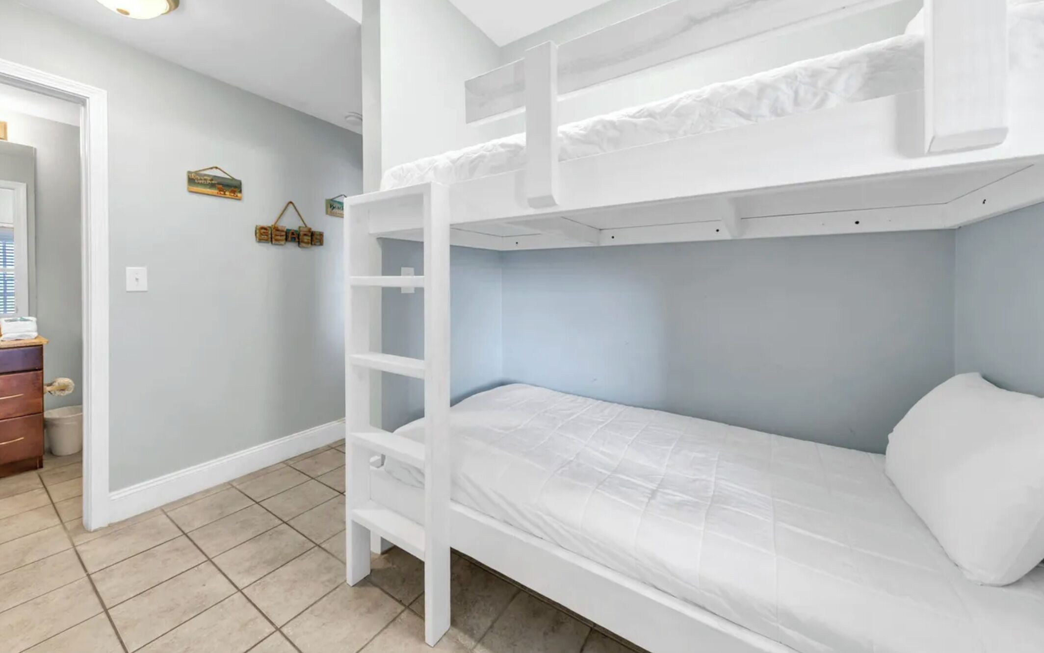 A bunk bed with a ladder, a dresser, and a wall with a small shelf and a sign.
