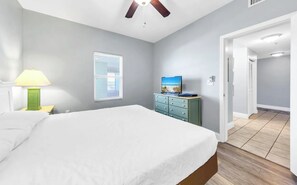 Et soveværelse med seng, kommode, fjernsyn, ventilator og et vindue med persienner.