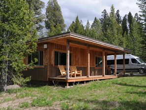 Une cabane dotée d’une terrasse en bois, d’un porche abrité et d’un véhicule garé à proximité.