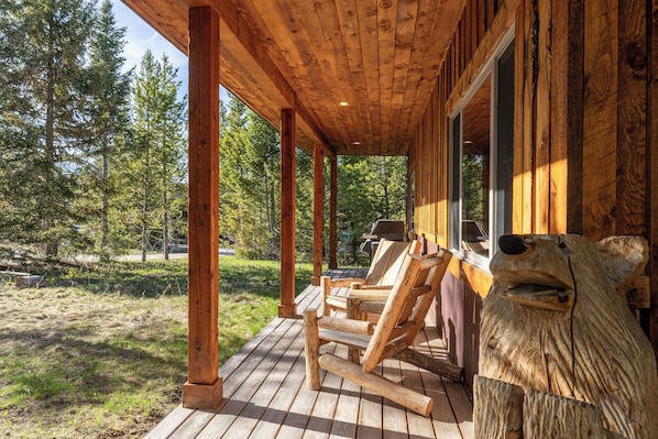 Eine Holzhütte mit Veranda, Sitzgelegenheit im Freien und einer Bärenskulptur.