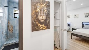 Ein Schlafzimmer mit einem Bett, einem Nachttisch, einem an der Wand montierten Fernseher und einem Gemälde eines Löwen.