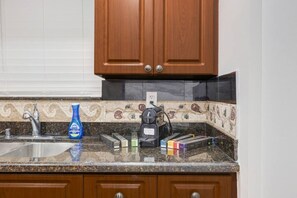 A kitchen with wooden cabinets, a granite countertop, a coffee maker, and a bottle of Dawn dish soap. - Pool + Hot Tub | Outdoor Kitchen | Hollywood FL (Hollywood)