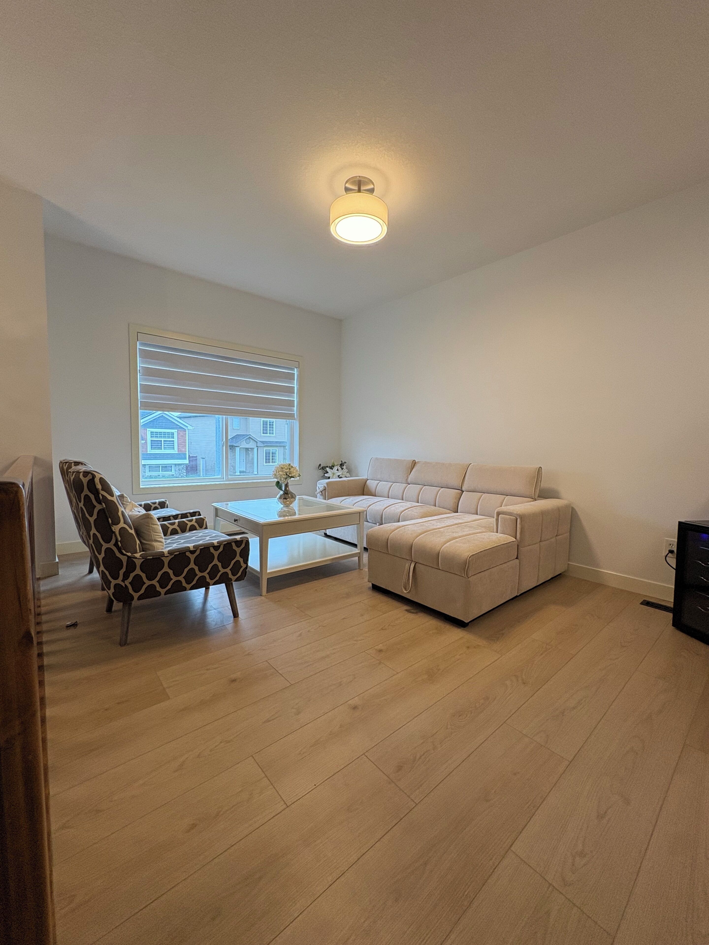 A living room with a sofa, a patterned armchair, a coffee table, and a window with blinds.