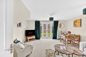 Ein Wohnzimmer mit Fernseher, Sofa, Couchtisch, Esstisch, Stühlen und Blick durch Glastüren.