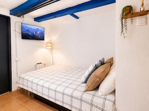 A bedroom with a bed, a TV mounted on the wall, a lamp, and a shelf with plants. - Gotico beach (Barcelona)