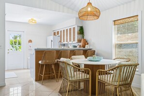 Eine Küche mit Essbereich, ausgestattet mit Rattanmöbeln, einer weißen Arbeitsplatte und einer Pendelleuchte.