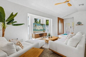 Ein modernes Wohnzimmer mit großem Fernseher, weißen Sofas, einem Holztisch und einer großen Pflanze.