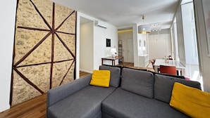 A modern living room with a sectional sofa, a stone accent wall, and a dining area in the background. - Lux Old Town (Lisboa)