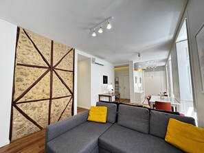 A modern living room with a sectional sofa, a stone accent wall, and a dining area in the background. - Lux Old Town (Lisboa)