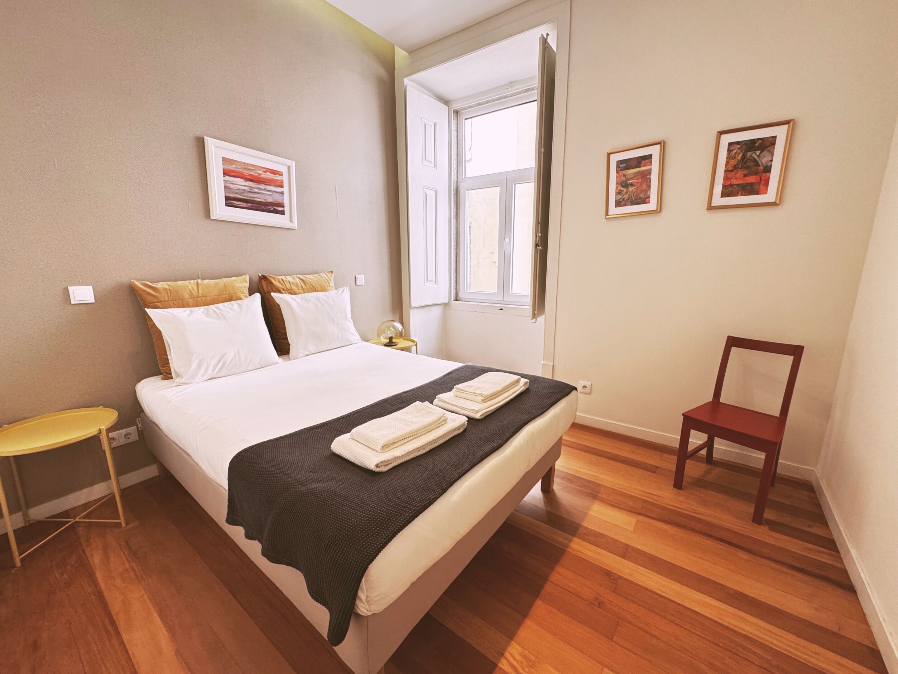 Een slaapkamer met een bed, een stoel, een nachtkastje en een raam.