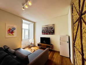 A living room with a sofa, a television, a small table, and a refrigerator. - Lux Old Town (Lisboa)