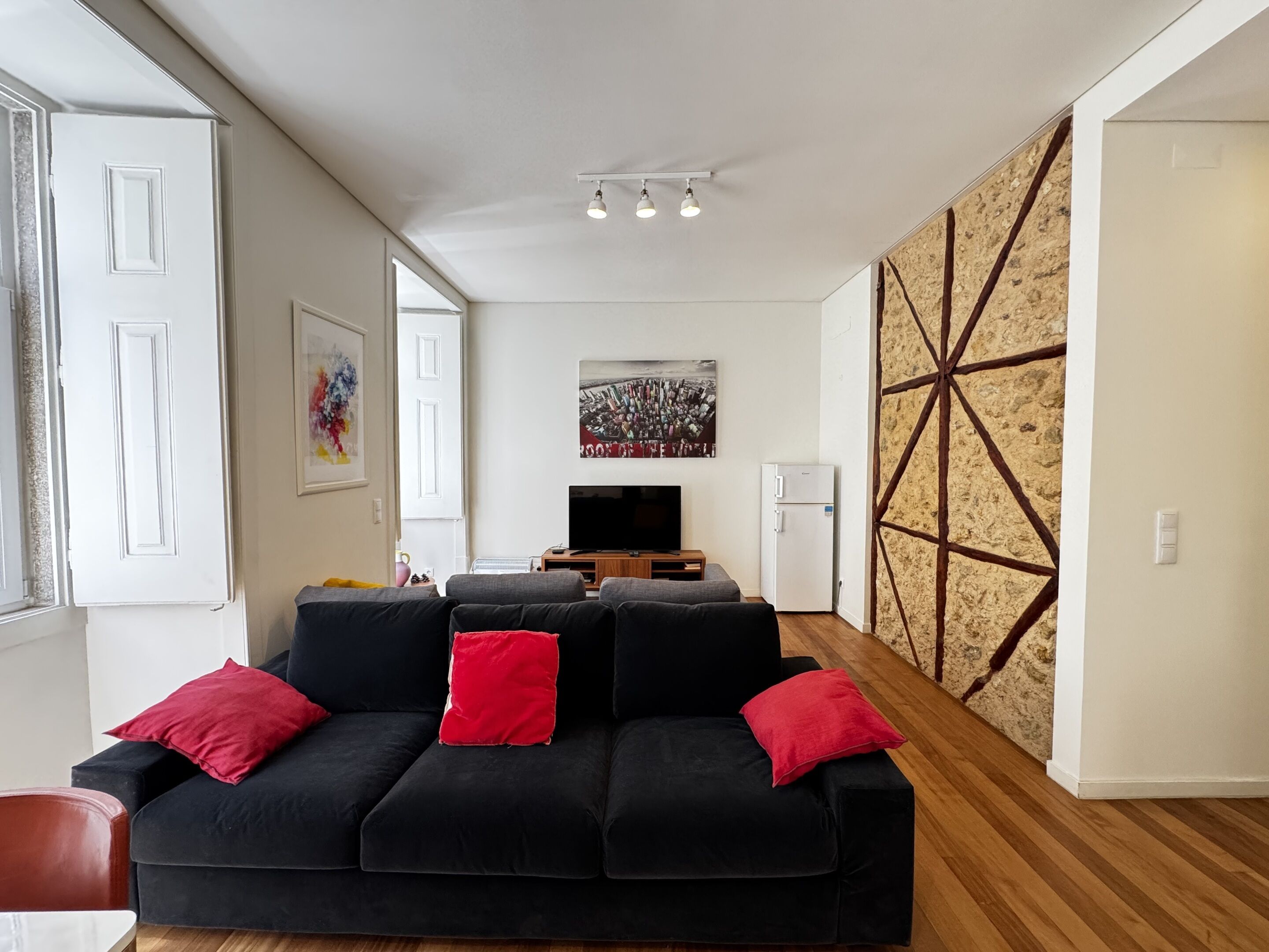 Een woonkamer met een zwarte bank, rode kussens, een flatscreen televisie en een muur met een geometrisch patroon.