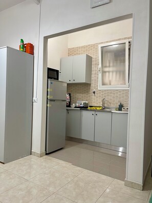 Eine Küche mit Kühlschrank, Mikrowelle, Schränken und einem Fenster.