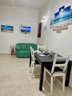 Ein Essbereich mit Tisch, Stühlen, einer grünen Couch, einem Fernseher und Wandbildern.