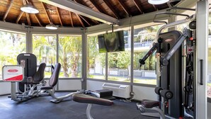 Ein Fitnessraum mit Trainingsgeräten, großen Fenstern und Blick auf Grünflächen.