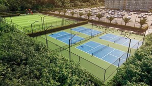 Ein Tennisplatzkomplex mit mehreren Plätzen, umgeben von einem Parkplatz und einem Gebäude im Hintergrund.
