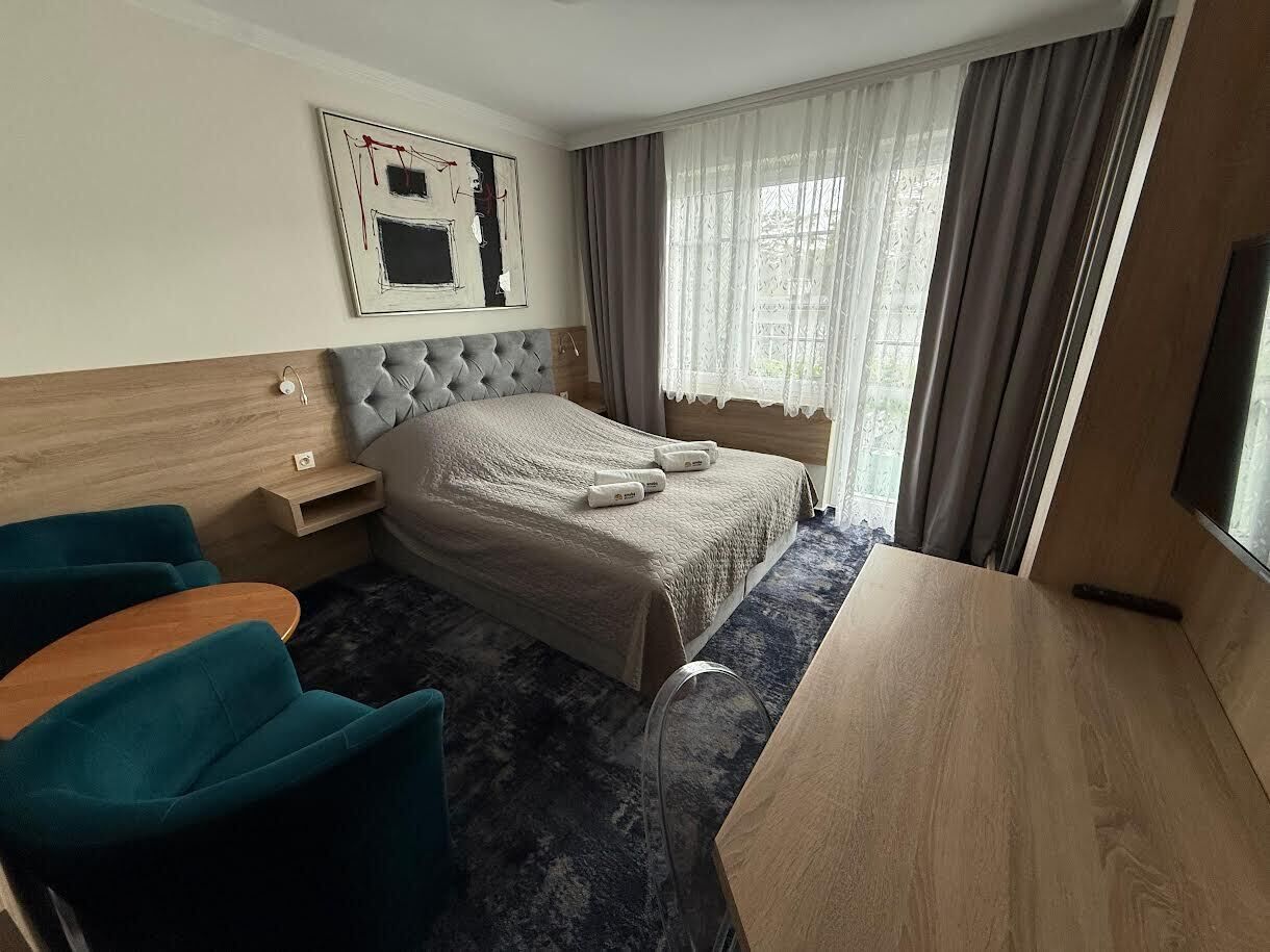 Een hotelkamer met een bed, een bureau, twee stoelen, een nachtkastje en een raam met gordijnen.