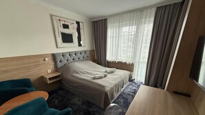 Ein Hotelzimmer mit einem Bett, einem Schreibtisch, zwei Stühlen, einem Nachttisch und einem Vorhangfenster.