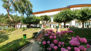 Ein Gebäude mit weißer Fassade, ein Ziegelweg, der zum Eingang führt, und ein Garten mit rosa Blumen.
