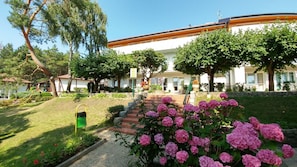 Ein Gebäude mit weißer Fassade, ein Ziegelweg, der zum Eingang führt, und ein Garten mit rosa Blumen.