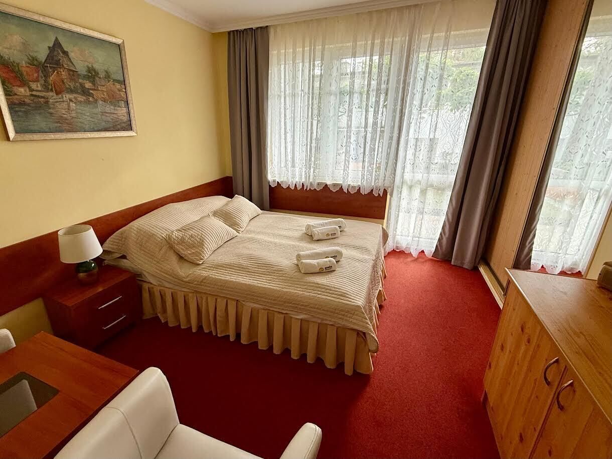A hotel room with a bed, a desk, a chair, a wooden dresser, and a painting on the wall.