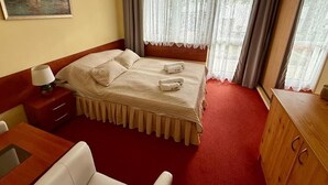 Ein Hotelzimmer mit Bett, Schreibtisch, Stuhl, einer Holzkommode und einem Bild an der Wand.