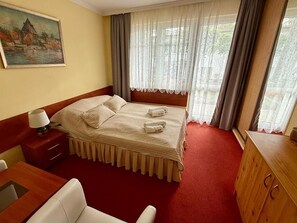 Ein Hotelzimmer mit Bett, Schreibtisch, Stuhl, einer Holzkommode und einem Bild an der Wand.
