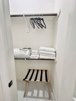 Ein Badezimmer mit Handtuchhalter, Ablagefläche mit gefalteten Handtüchern und einem Wäscheständer.
