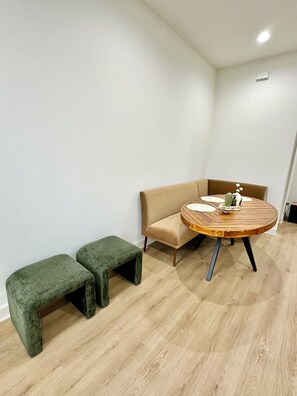 Ein Zimmer mit einem runden Holztisch, einem beigefarbenen Sofa und zwei grünen Hocker.
