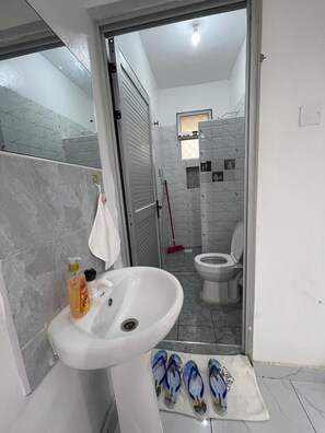 Ein Badezimmer mit weißem Waschbecken, Spiegel, Toilette und Duschbereich.