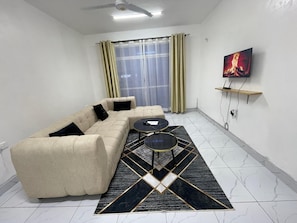 Ein Wohnzimmer mit Ecksofa, Couchtisch, an der Wand montiertem Fernseher und einem gemusterten Teppich.