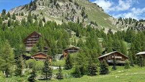 A mountain lodge with multiple wooden cabins, surrounded by dense forest and a prominent rocky peak in the background. - Luxury apartment, South-facing terrace, Exceptional view, Lock-up garage (Isola)