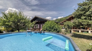A swimming pool with a wooden deck, a lifeguard chair, and a building in the background. - Mazot des Outards - Swimming pool - Air conditioning - Cozy garden (Passy)