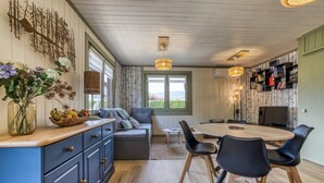 A modern kitchen with a dining area, wooden cabinets, a sofa, and a view through the window. - Mazot des Outards - Swimming pool - Air conditioning - Cozy garden (Passy)