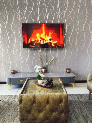 Uma sala de estar com televisão de tela plana na parede, sofá, mesa de centro com objetos decorativos e parede estampada.