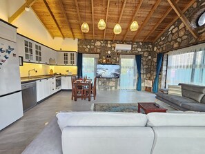 Eine moderne Küche mit weißen Schränken, ein Essbereich mit Tisch und Stühlen, ein Wohnzimmer mit Sofa und Couchtisch sowie eine Steinwand.