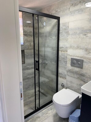Ein modernes Badezimmer mit Duschkabine aus Glas, einer weißen Toilette und einem integrierten Waschbecken.
