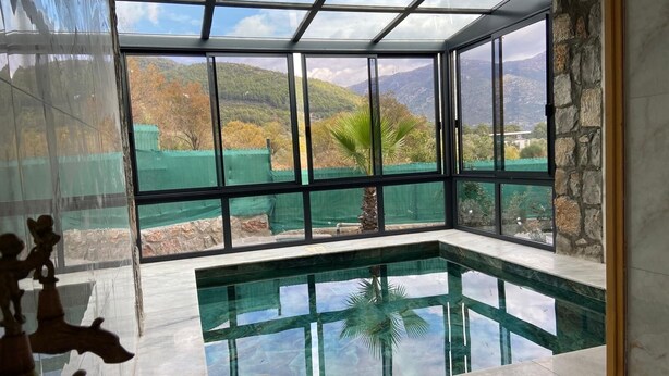 Ein modernes Interieur mit einem gläsernen Pool, Steinwänden und Blick auf eine gebirgige Landschaft.