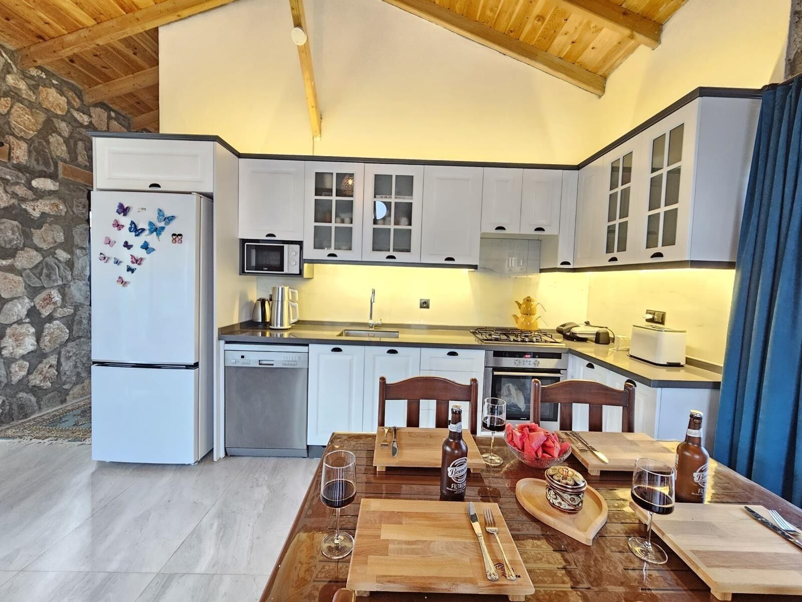 A kitchen with white cabinets, a microwave, a stove, and a dining table set with wine glasses and bottles.