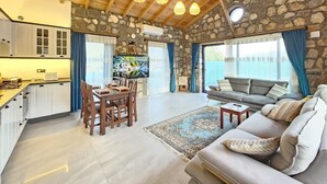 Ein geräumiger Wohnbereich mit Steinwand, Holzbalkendecke, einem Esstisch und einer Couch.