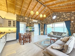 A spacious living area with a stone wall, wooden ceiling beams, a dining table, and a sofa.