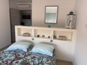 Une chambre à coucher comprenant un lit, un miroir, des étagères ornées d’objets décoratifs et un appareil de climatisation.