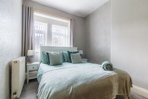 Een slaapkamer met een bed, nachtkastjes, een raam met gordijnen en een radiator.